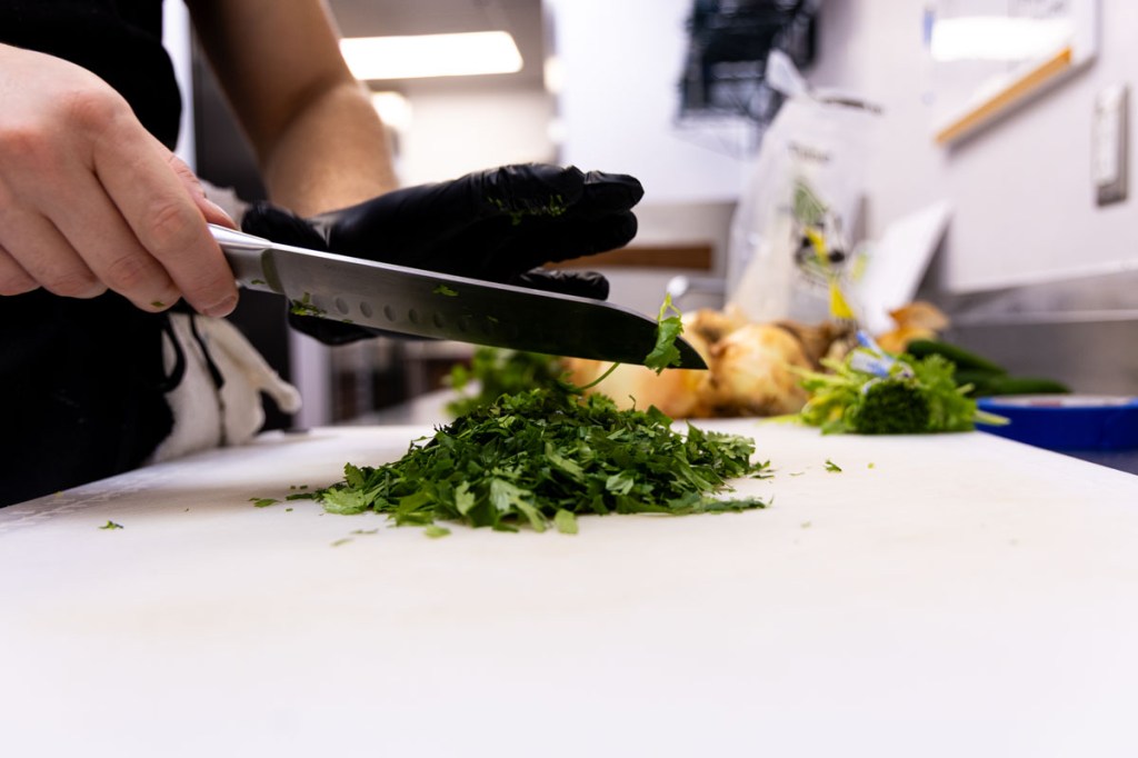 A cook wipes cilantro off of his knife into a pile of it below.