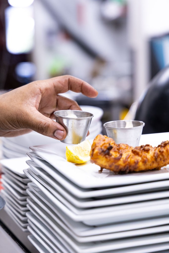 A chef placing a ramekin of tarter sauce onto a plate.